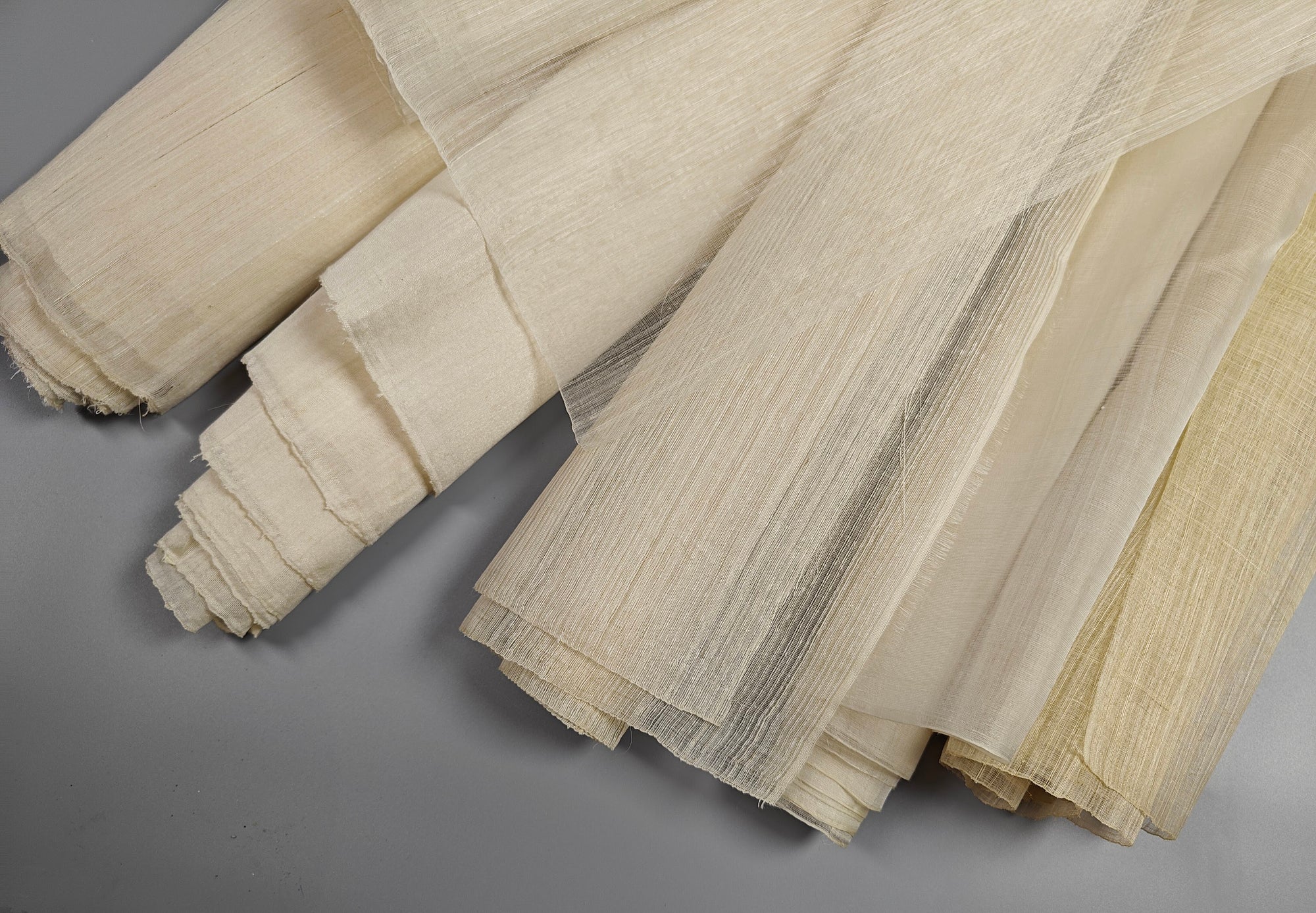 Handwoven natural fabric rolls arranged on a gray background by Manila Designer authentic Philippine Textiles