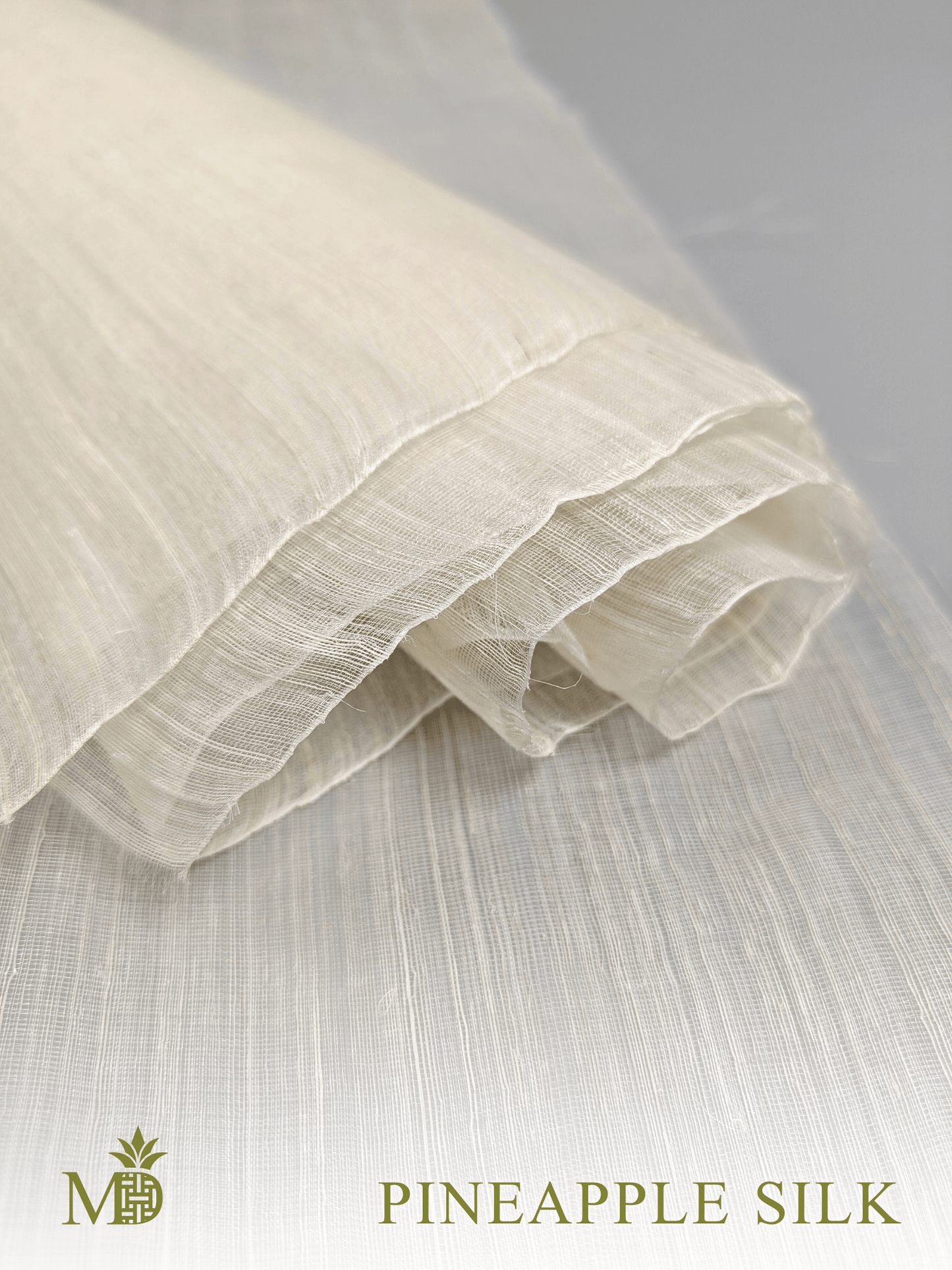 Close-up of rolled Philippine natural pineapple silk pina silk fabric on a light grey background by Manila Designer, handwoven sustainable textiles from the Philippines