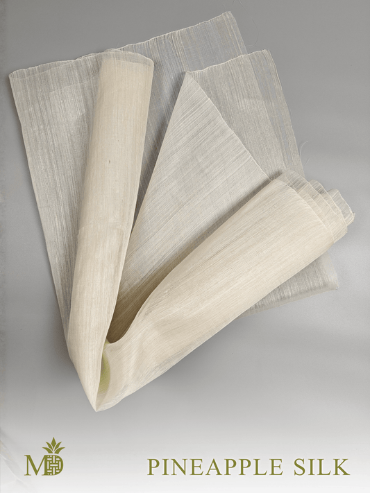 Rolled and folded Philippine natural pineapple silk or pina silk fabric on a grey background by Manila Designer, handwoven sustainable textiles from the Philippines